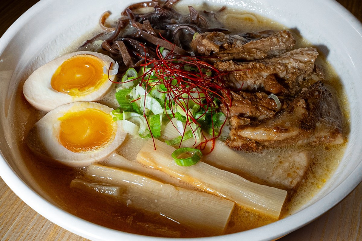 A steaming bowl of authentic Tonkotsu Ramen with pork bone broth, topped with chashu pork belly, a seasoned nitamago egg, wood ear mushrooms and chives at 107 Taste restaurant in Miami.
