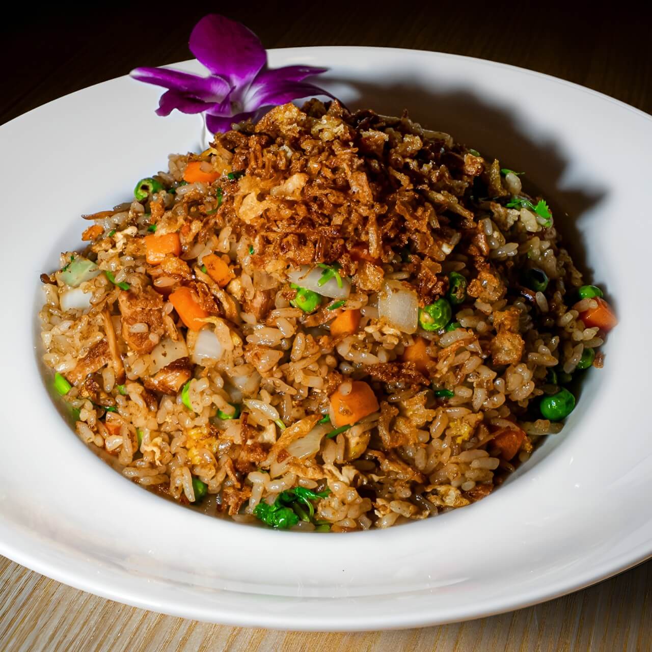 A hearty serving of Mama pork Fried Rice topped with crispy shallots, mixed vegetables, and a purple orchid garnish at 107 Taste.